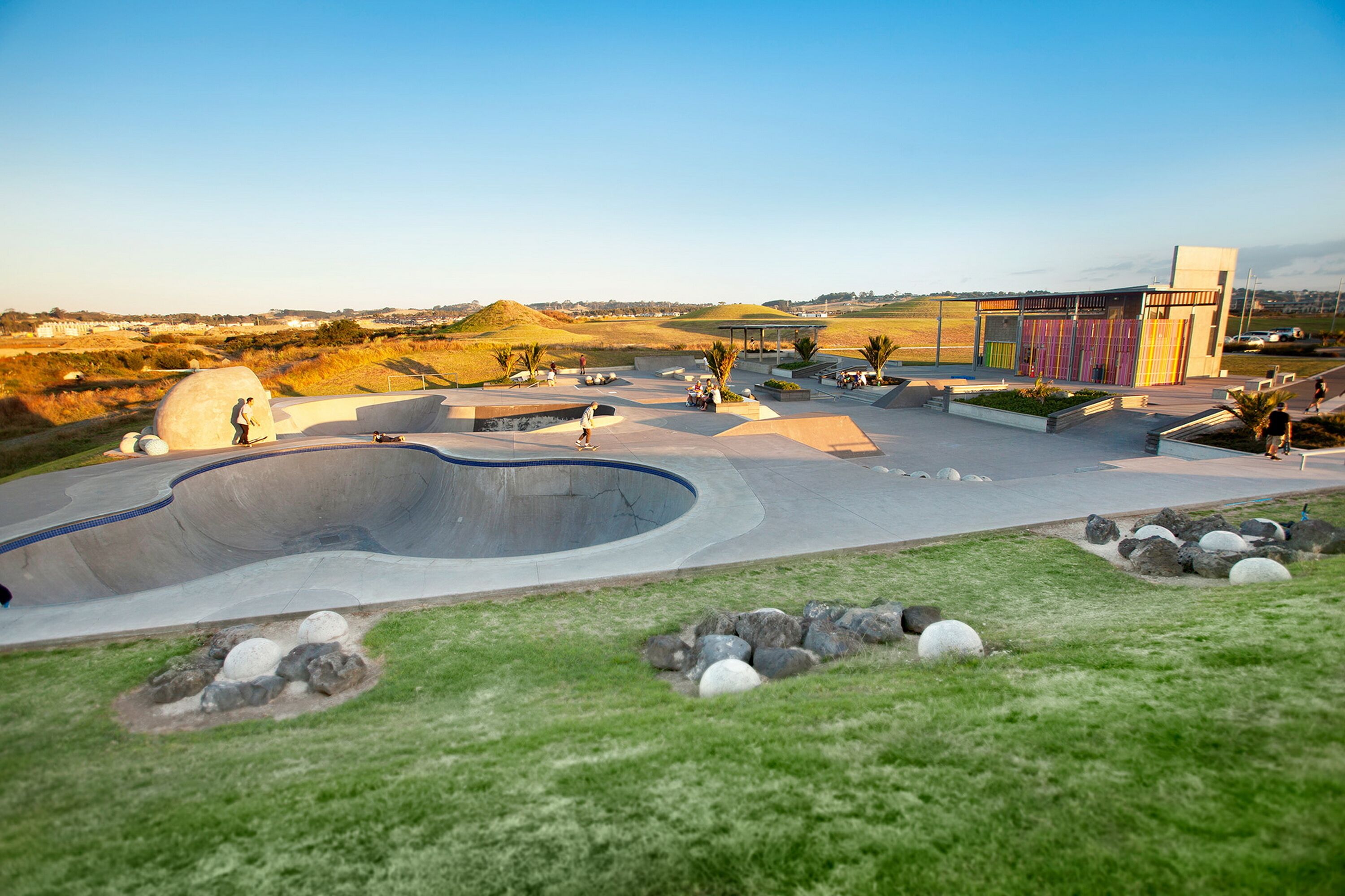 Ein Skatepark mit einer großen Halfpipe, Sitzbereichen und einem Gebäude mit farbenfrohen Verkleidungen.