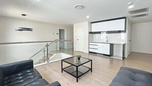 A modern living room with a glass coffee table, leather sofas, and a kitchen area with white cabinets and a marble backsplash. - Koromeke Luxury 370sqm New Build– Ideal for Groups (Auckland)