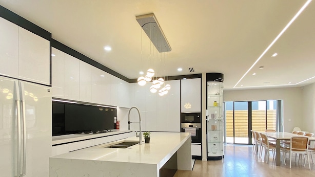 A modern kitchen with a central island, stainless steel appliances, and a dining area with wooden flooring and a glass partition. - Koromeke Luxury 370sqm New Build– Ideal for Groups (Auckland)