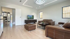 A modern living room with a flat-screen TV, leather sofas, a glass coffee table, and a chandelier. - Koromeke Luxury 370sqm New Build– Ideal for Groups (Auckland)