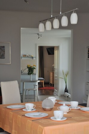 Ein Essbereich mit einem Tisch für vier Personen, einer Blumenvase und einer sichtbaren Küche im Hintergrund.