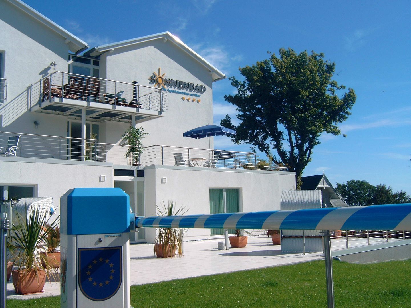 A modern building with a balcony, a flag, and potted plants.