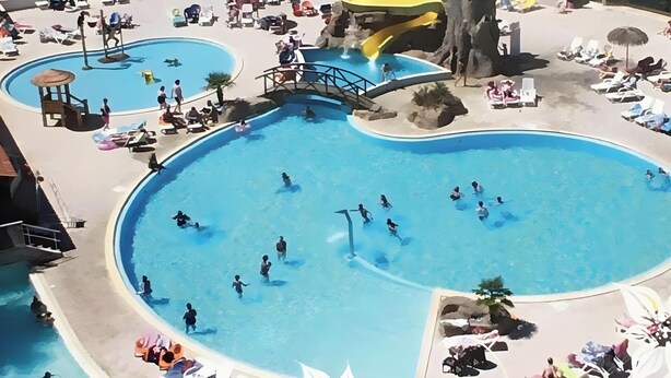 Una gran piscina exterior amb diverses línies, envoltada de gandules i ombrelles.