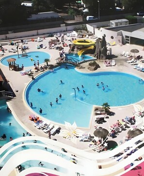 Una amplia piscina al aire libre con varias pistas de natación, rodeada de sillas de descanso y sombrillas.