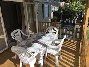 Eine überdachte Terrasse mit Tisch, Stühlen, einem Grill und einer Schiebetür zum Haus.