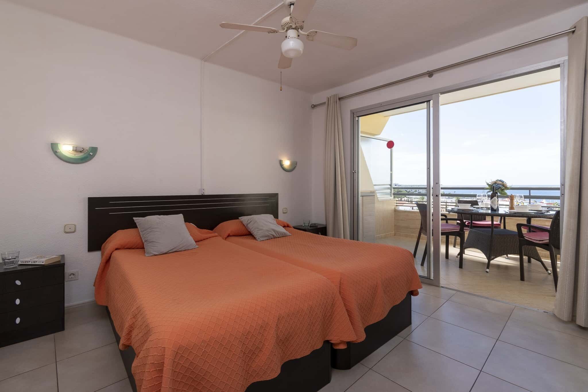Ein Hotelzimmer mit einem großen Bett, einem Deckenventilator, einem Nachttisch und Blick auf den Balkon mit Sitzgelegenheit.