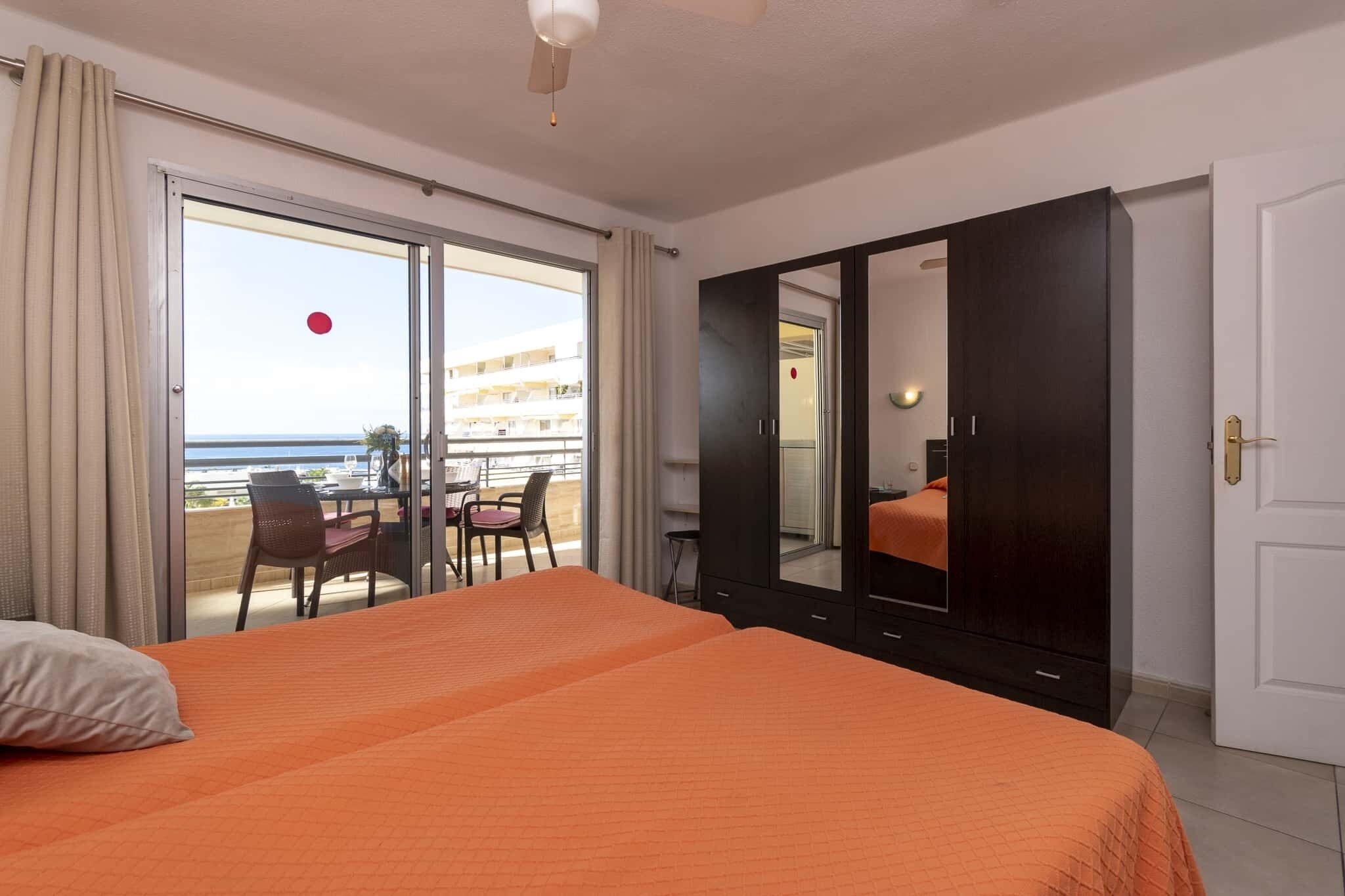 A hotel room with two beds, a large mirror, and a sliding glass door leading to a balcony with a view of the sea.