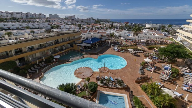 Un resort con una grande piscina, diverse aree relax e vista sul mare.