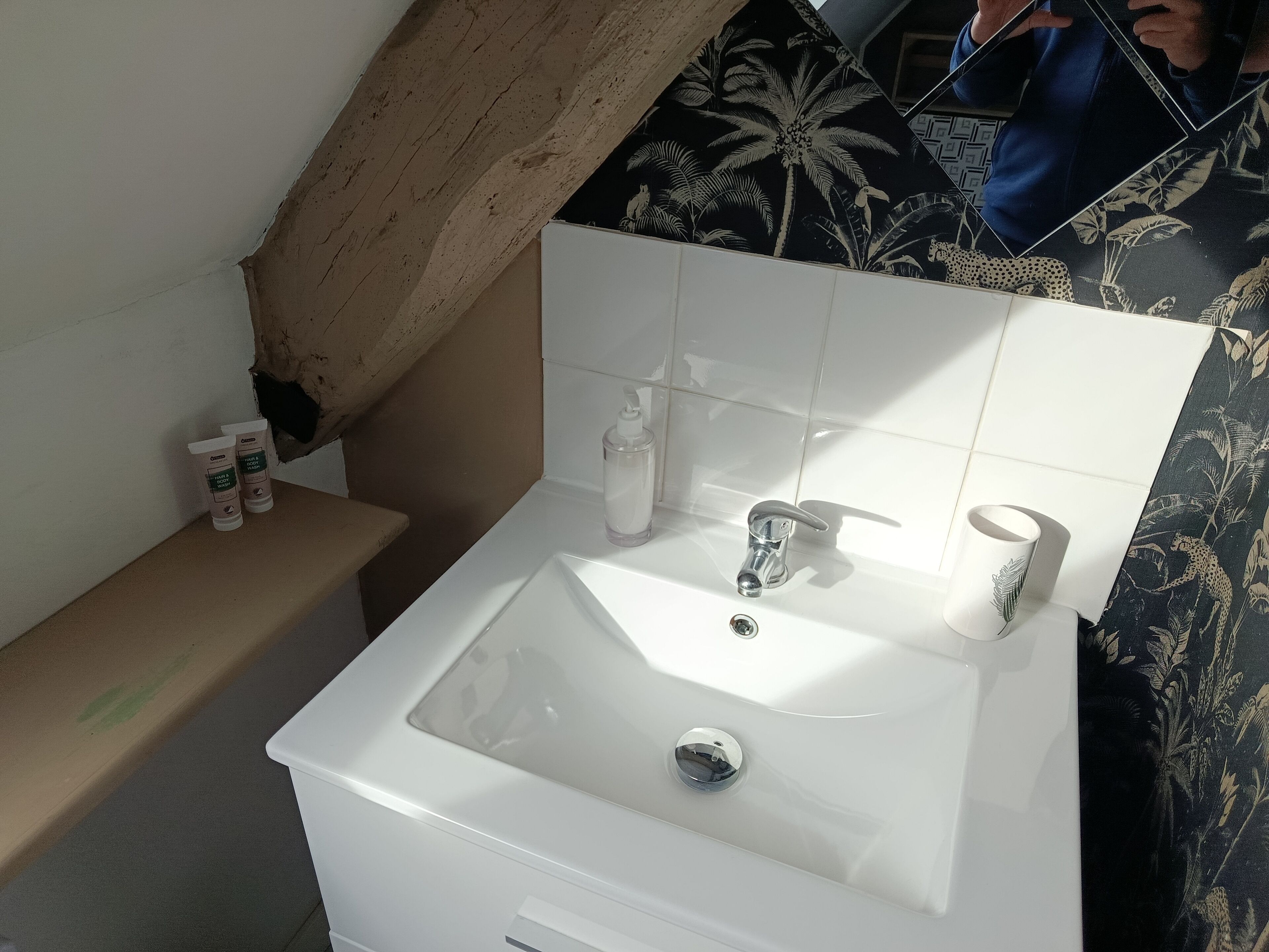 Un bany amb un lavabo blanc, un mirall i productes de tocador a l'estant.