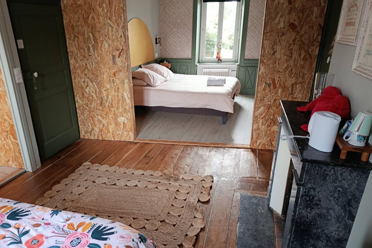 A bedroom with a bed, a window, a radiator, and a small table with a kettle and cups.