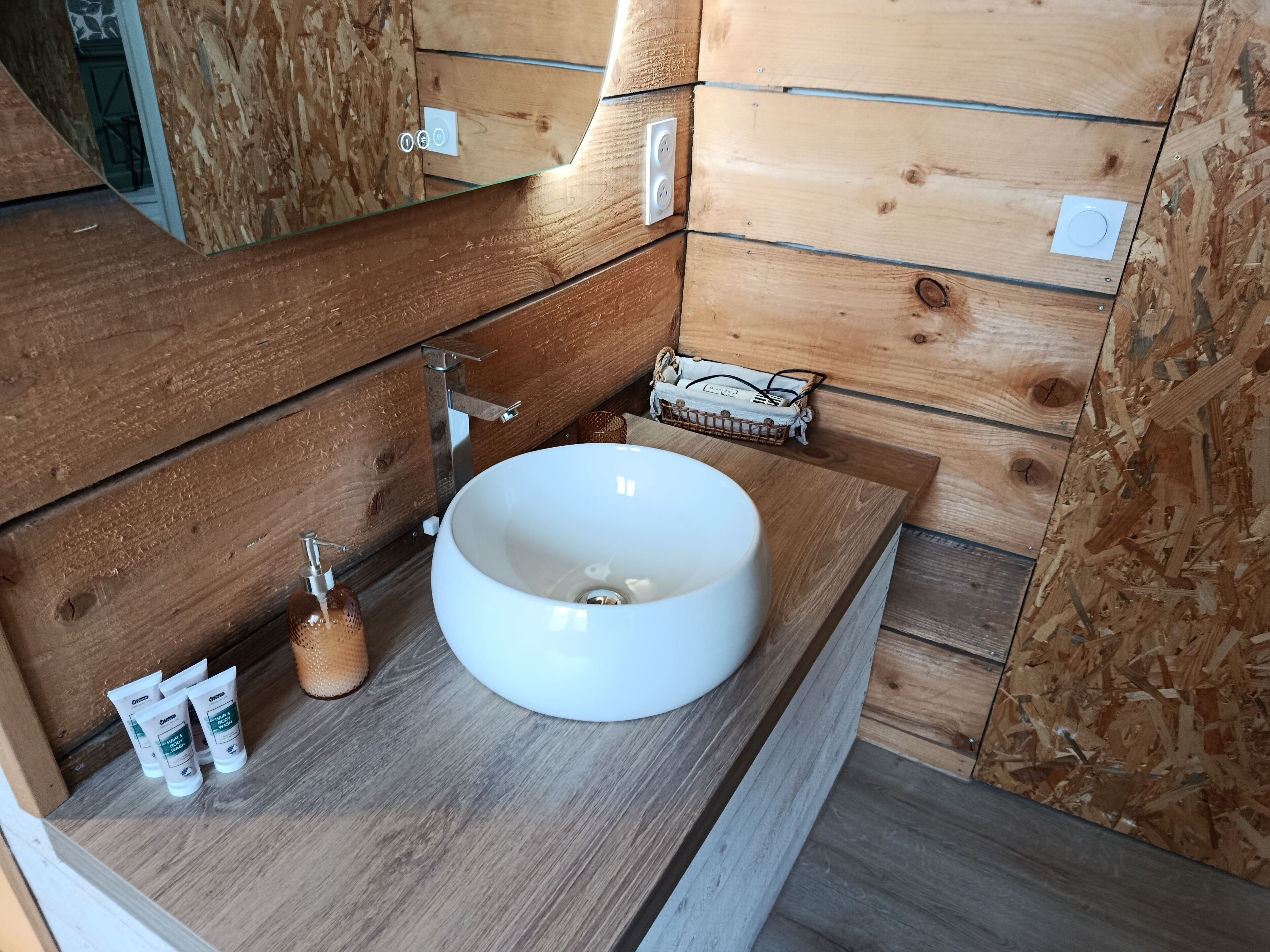 A wooden bathroom with a large white sink, a mirror, and a small shelf with toiletries.