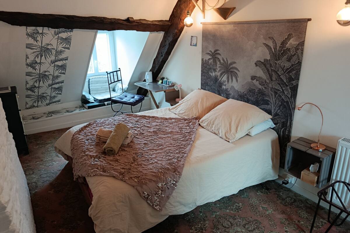 A bedroom with a large bed, a chair, a desk, and a window.