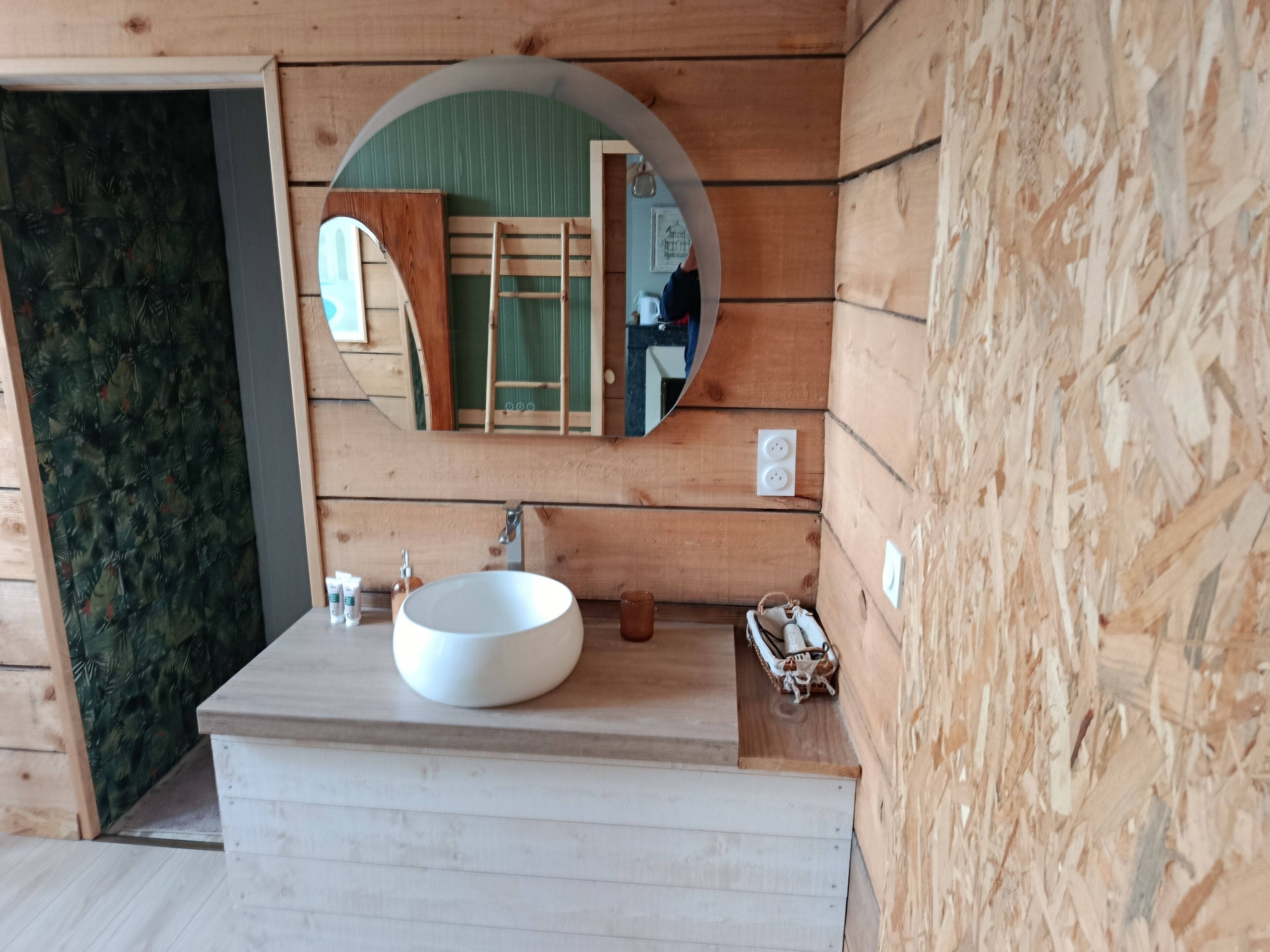 A wooden cabin bathroom with a round mirror, a white sink, and a ladder against the wall.