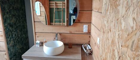 A wooden cabin bathroom with a round mirror, a white sink, and a ladder against the wall.