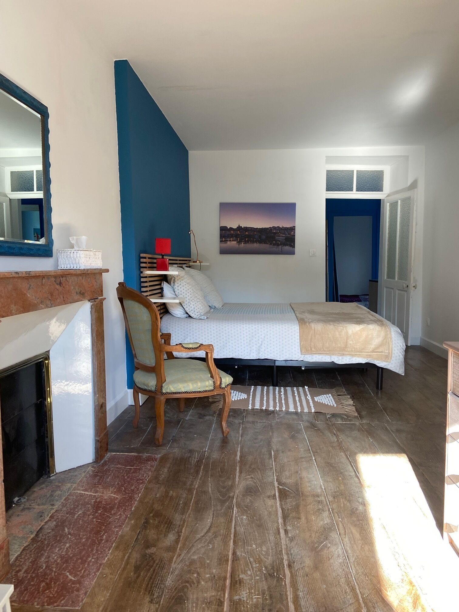 Ein Schlafzimmer mit Bett, einem Sessel, einem Kamin, einem Gemälde und einer Tür.
