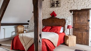 A bedroom with a stone wall, a wooden bed frame, and a red and beige bedspread. - Atipyk'Ododo (Saint-James)