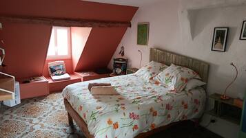 Un dormitorio con techo inclinado, una cama con ropa de cama floral, un sillón de lectura y una mesita de noche con lámpara.