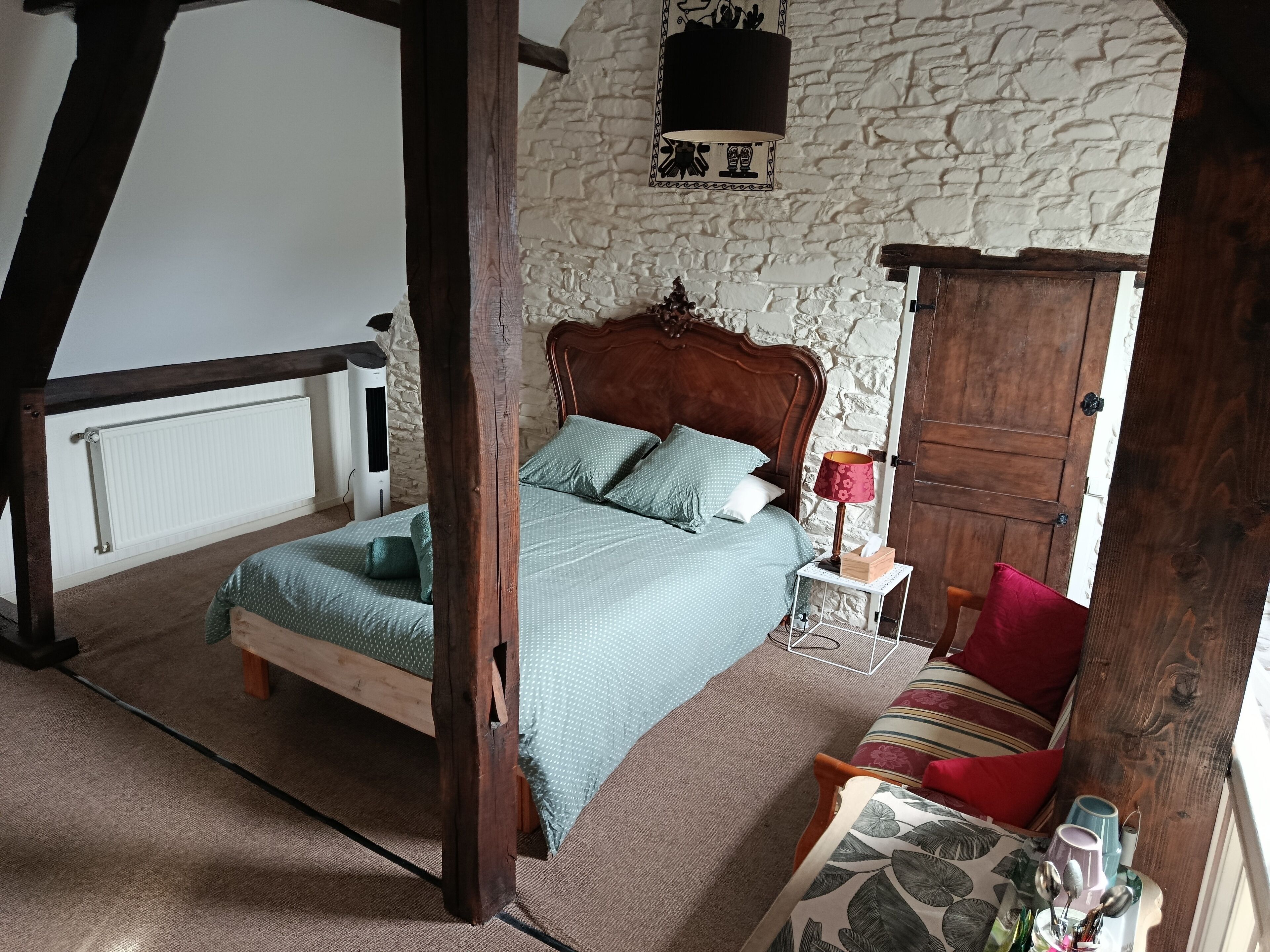 Een slaapkamer met een houten bed, een nachtkastje met een lamp, een rode kussens en een houten garderobe.