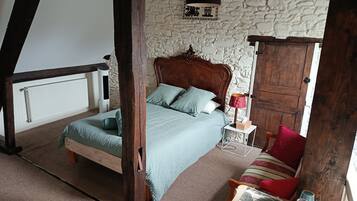 Een slaapkamer met een houten bed, een nachtkastje met een lamp, een rode kussens en een houten garderobe.