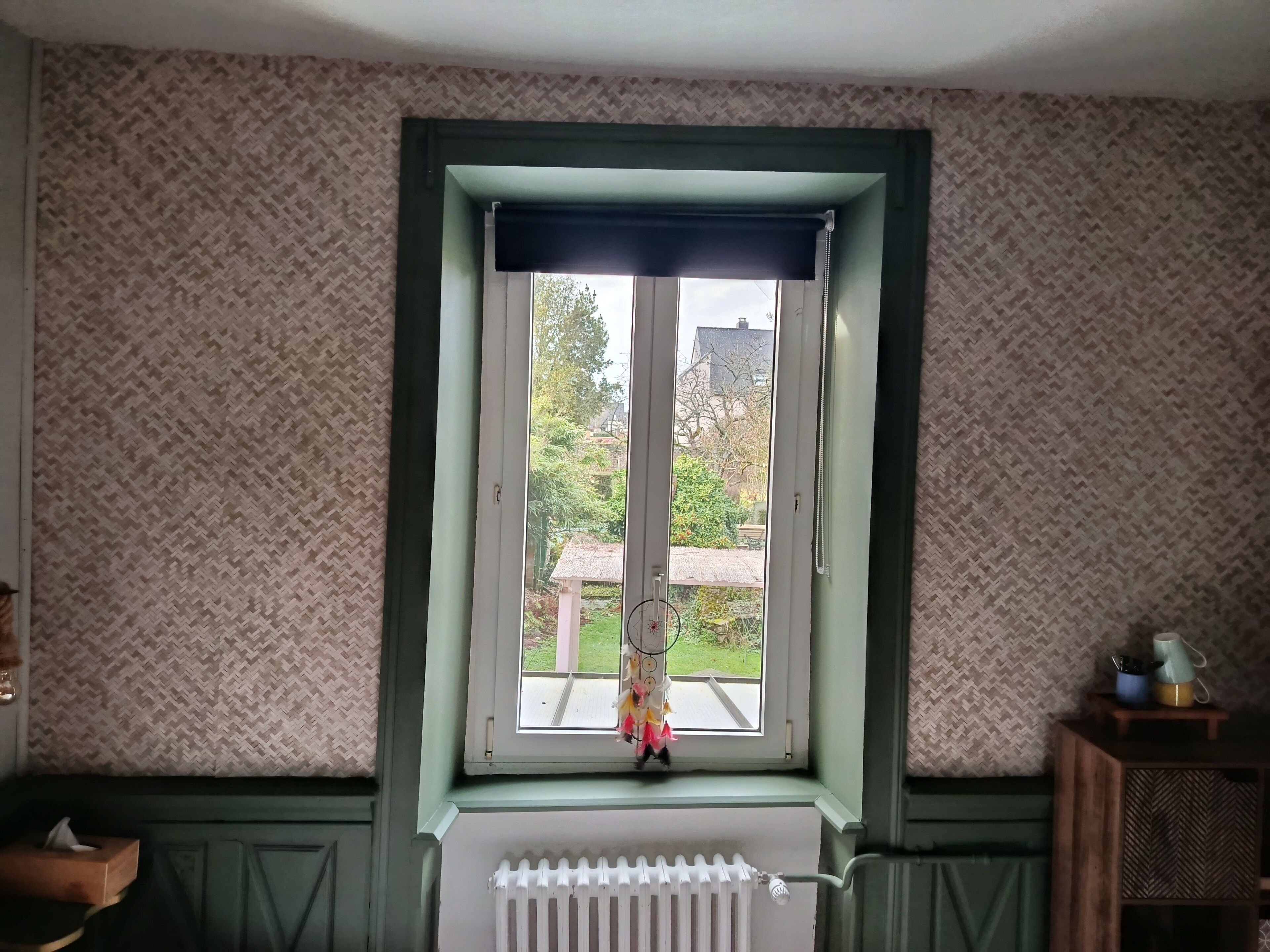 A room with a window, patterned wallpaper, a radiator, and a small wooden table with a cup and saucer.