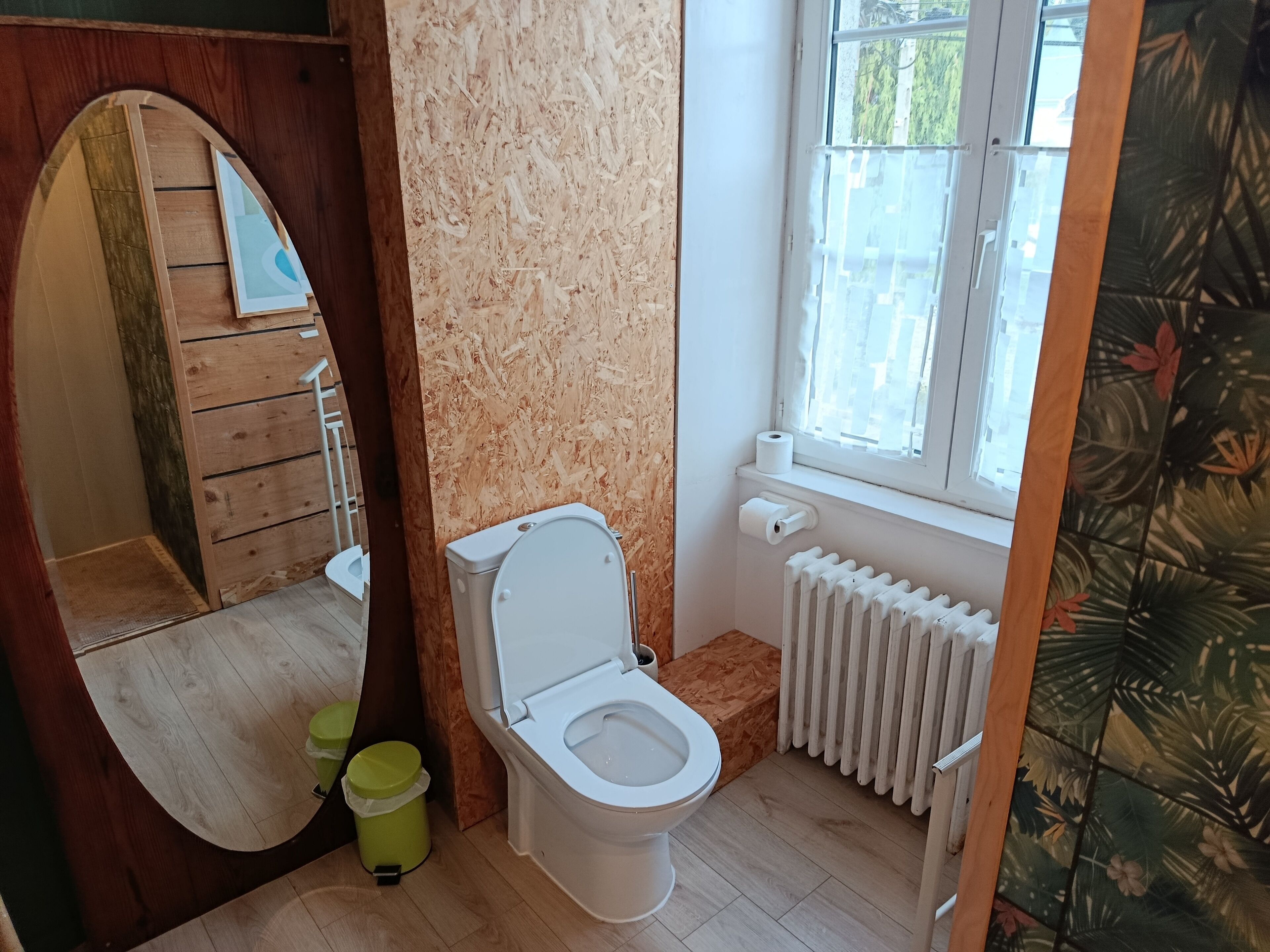Un baño con inodoro, radiador, ventana y espejo.