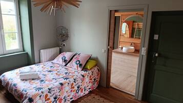 Un dormitorio con una colcha estampada con flores, suelo de madera, una puerta verde y vistas al baño.