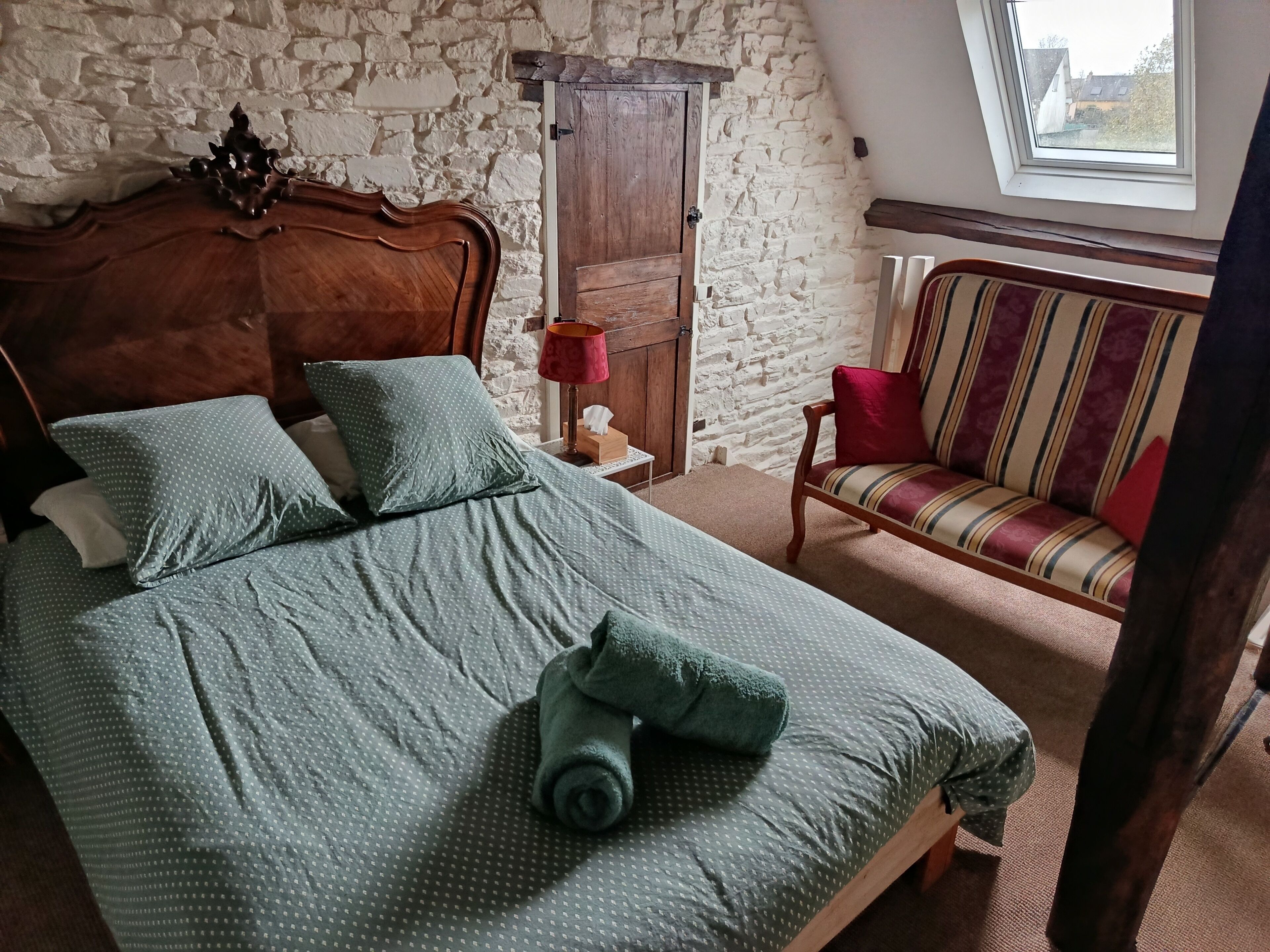 Une chambre avec un lit en bois, un canapé à rayures, un mur en pierre et une fenêtre.