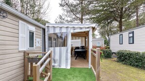 En campingvogn med et overdækket udendørsområde, en træterrasse og en lille have.