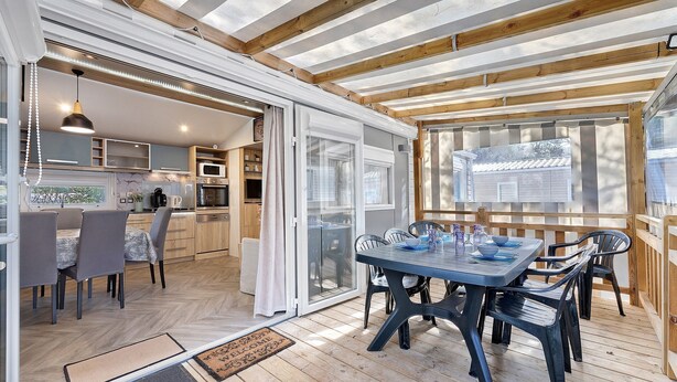 Et åbent køkken med spiseplads, træbjælker og en skydedør til en terrasse.