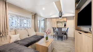 Et moderne interiør med en sofa, et lille bord med en vase, et spiseområde og et fjernsyn monteret på væggen.