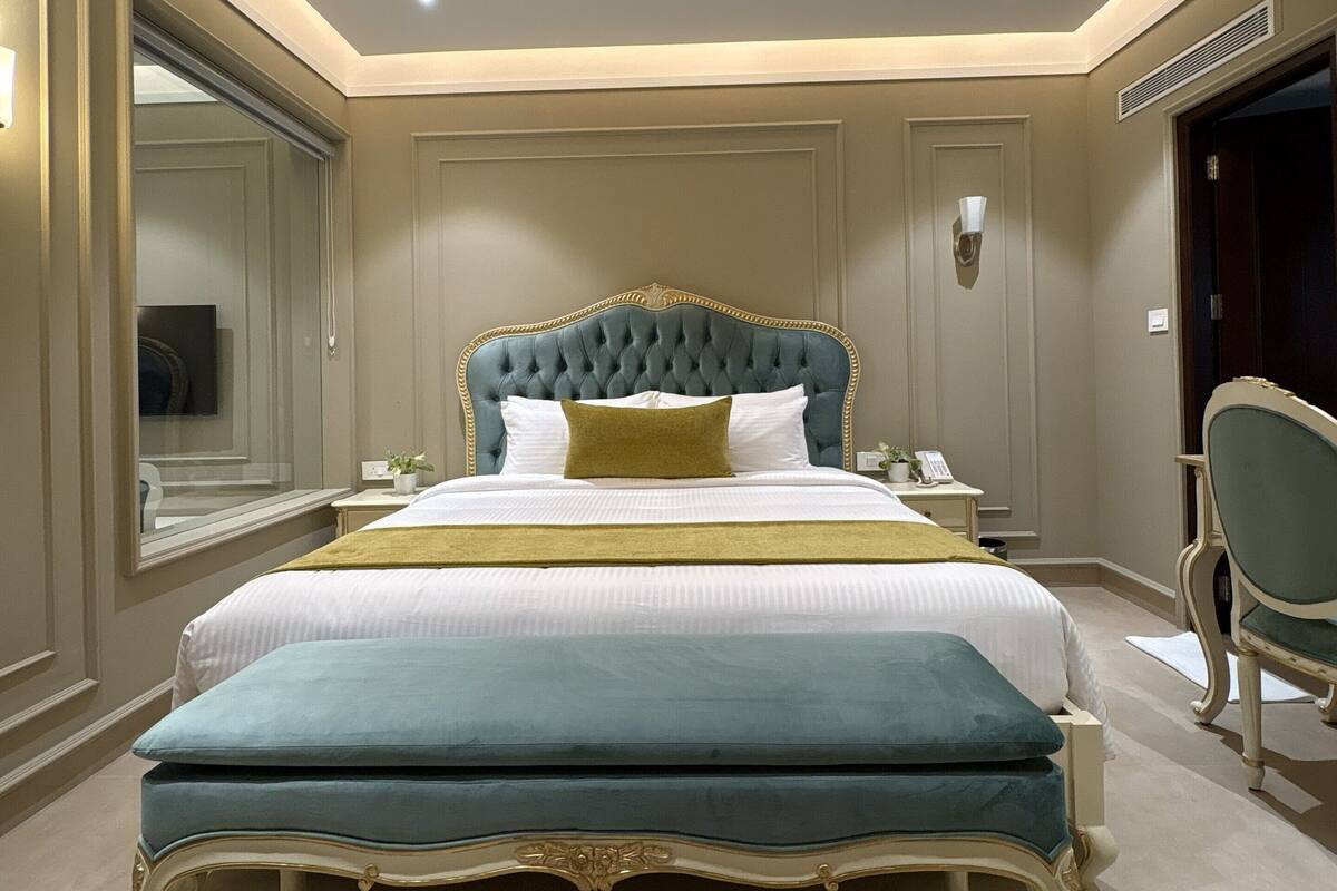 Una cama grande con cabecera capitonada, una mesita de noche con lámpara y una silla.