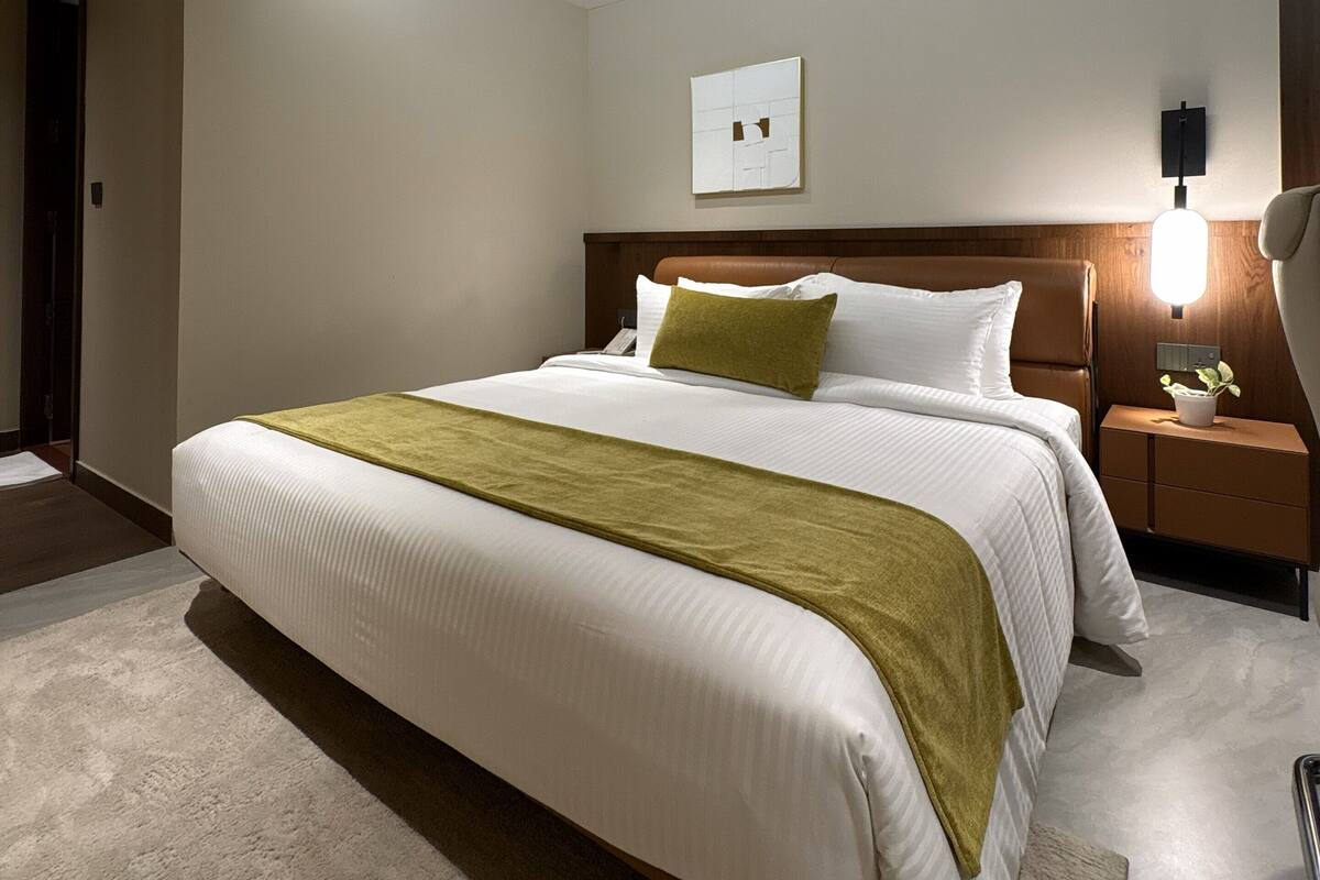Una habitación de hotel moderna con una cama grande, una mesita de noche con lámpara y una obra de arte colgada en la pared.