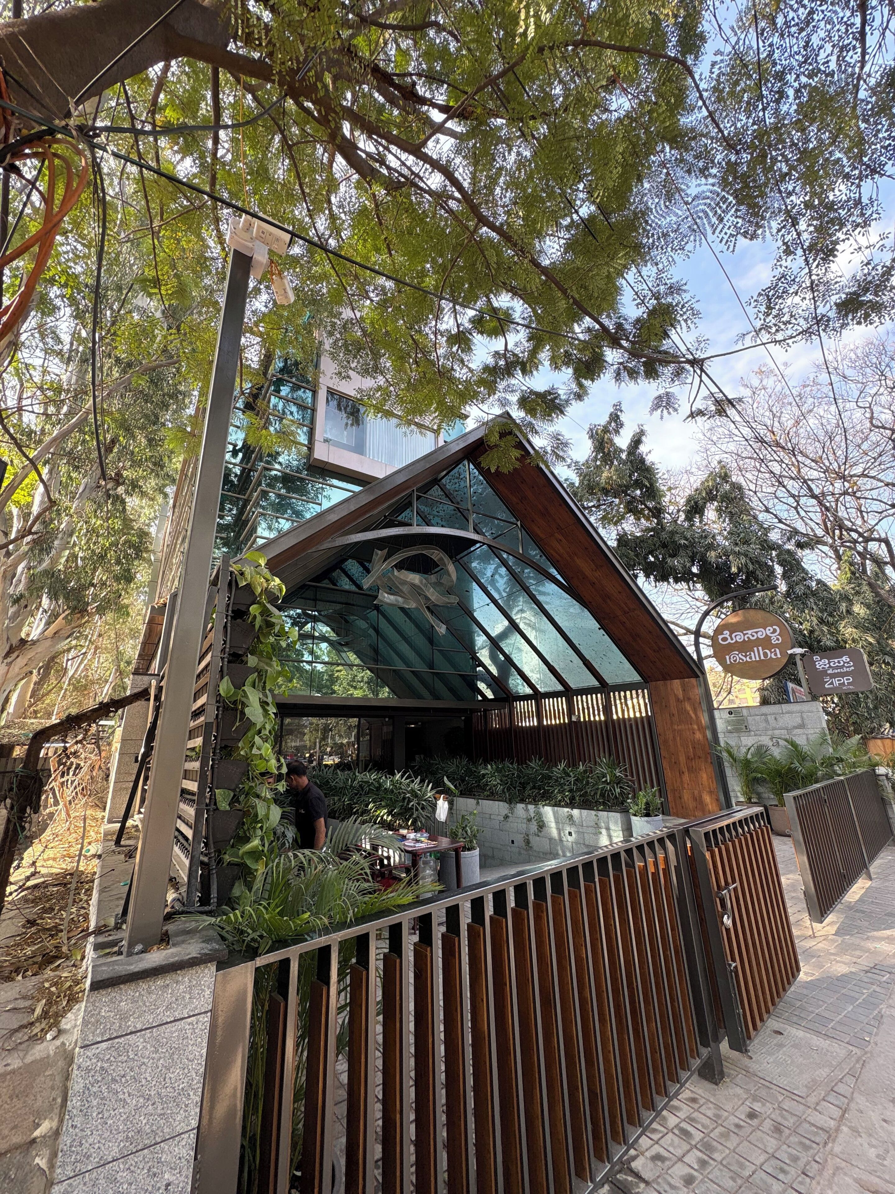 Un edificio moderno con fachada de vidrio, rodeado de vegetación y una cerca metálica.