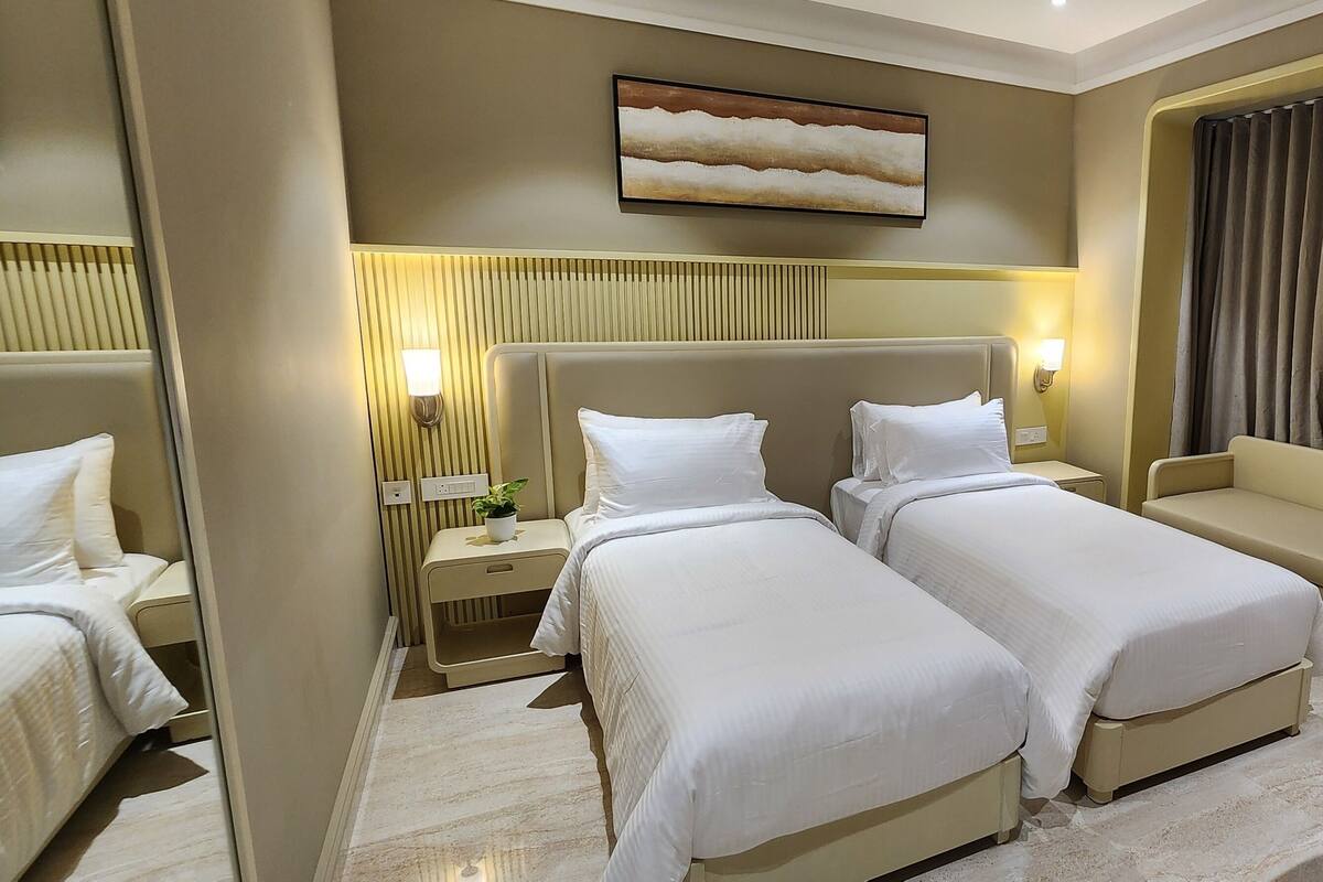Habitación de hotel con dos camas, un sofá, un ventanal con cortinas, una obra de arte colgada en la pared y lámparas de noche.