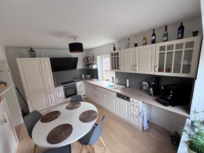 A compact kitchen with white cabinetry, a dining table with woven placemats, and a variety of bottles on the upper shelf. - Baltic Sea Lounge beautiful, bright large apartment 100sqm in Kühlungsborn (Kühlungsborn)