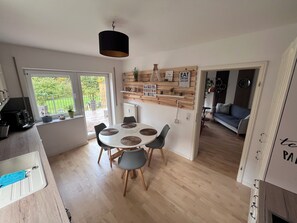 A modern kitchen with a dining area, wooden shelves with decorative items, and a view of the garden through the window. - Baltic Sea Lounge beautiful, bright large apartment 100sqm in Kühlungsborn (Kühlungsborn)