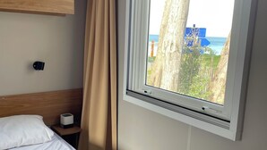 Ein Hotelzimmer mit Bett, Nachttisch, Lampe, Fenster mit Meerblick und einem hölzernen Kopfteil.