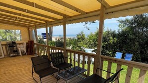 Eine überdachte Terrasse im Freien mit Holzboden, Metallstühlen, einem Tisch und einem Grill.
