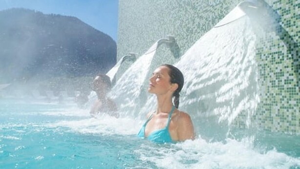 Une personne portant un maillot de bain bleu, se trouvant dans une installation aquatique avec une cascade en arrière-plan.