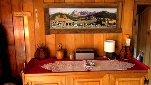 L’intérieur d’un chalet en bois, avec un tableau représentant un paysage de montagne accroché au mur, un meuble en bois doté de tiroirs, une radio et une table recouverte d’une nappe rouge.