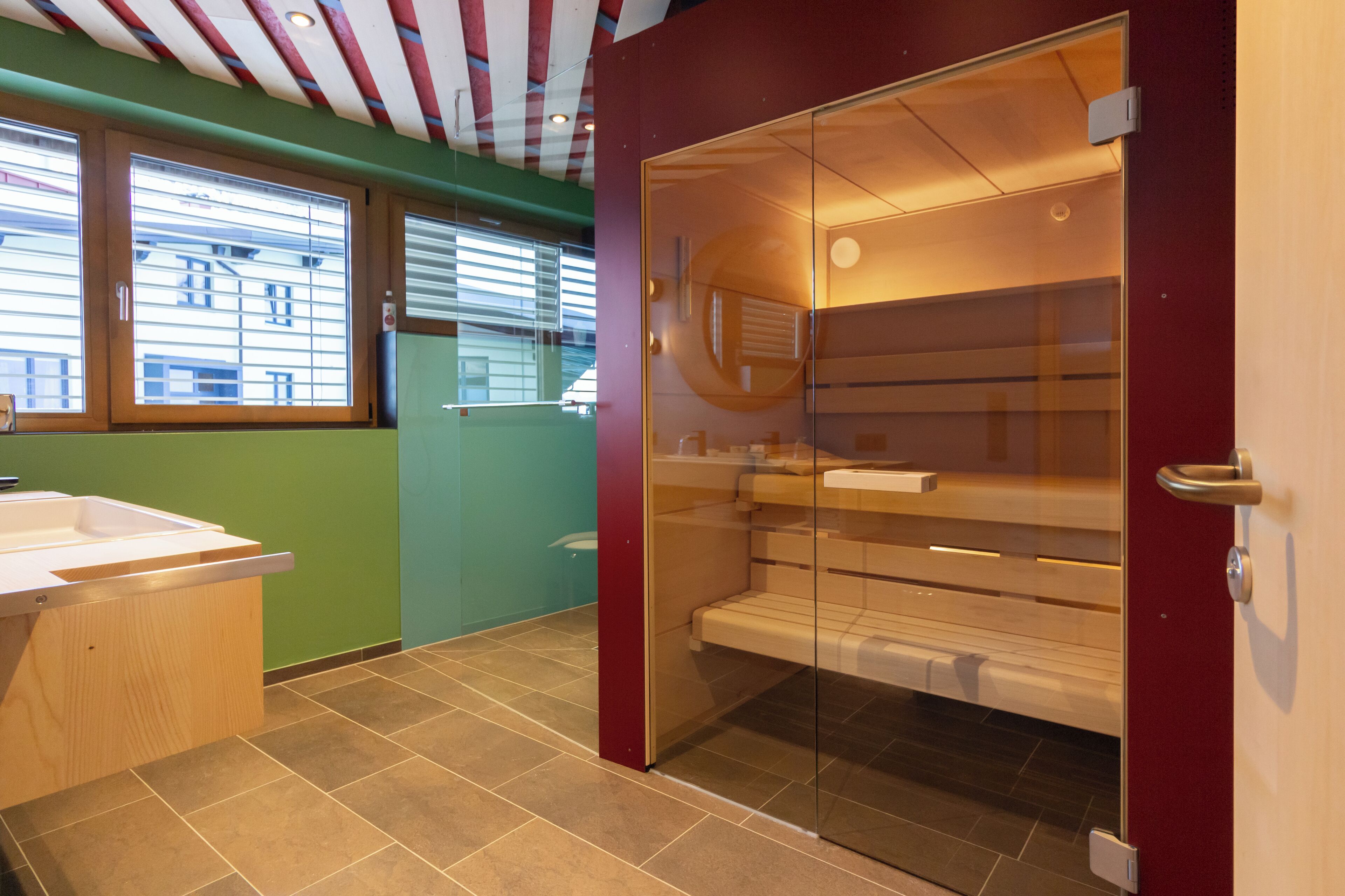 A modern bathroom with a glass shower enclosure, a wooden vanity, and a green accent wall.