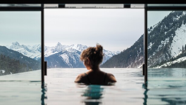 Una persona in piscina con vista su montagne innevate.