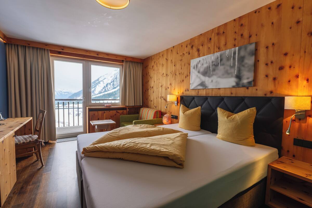 Ein Hotelzimmer mit Bett, Holzwänden, einem Gemälde, einem Schreibtisch und Bergblick.