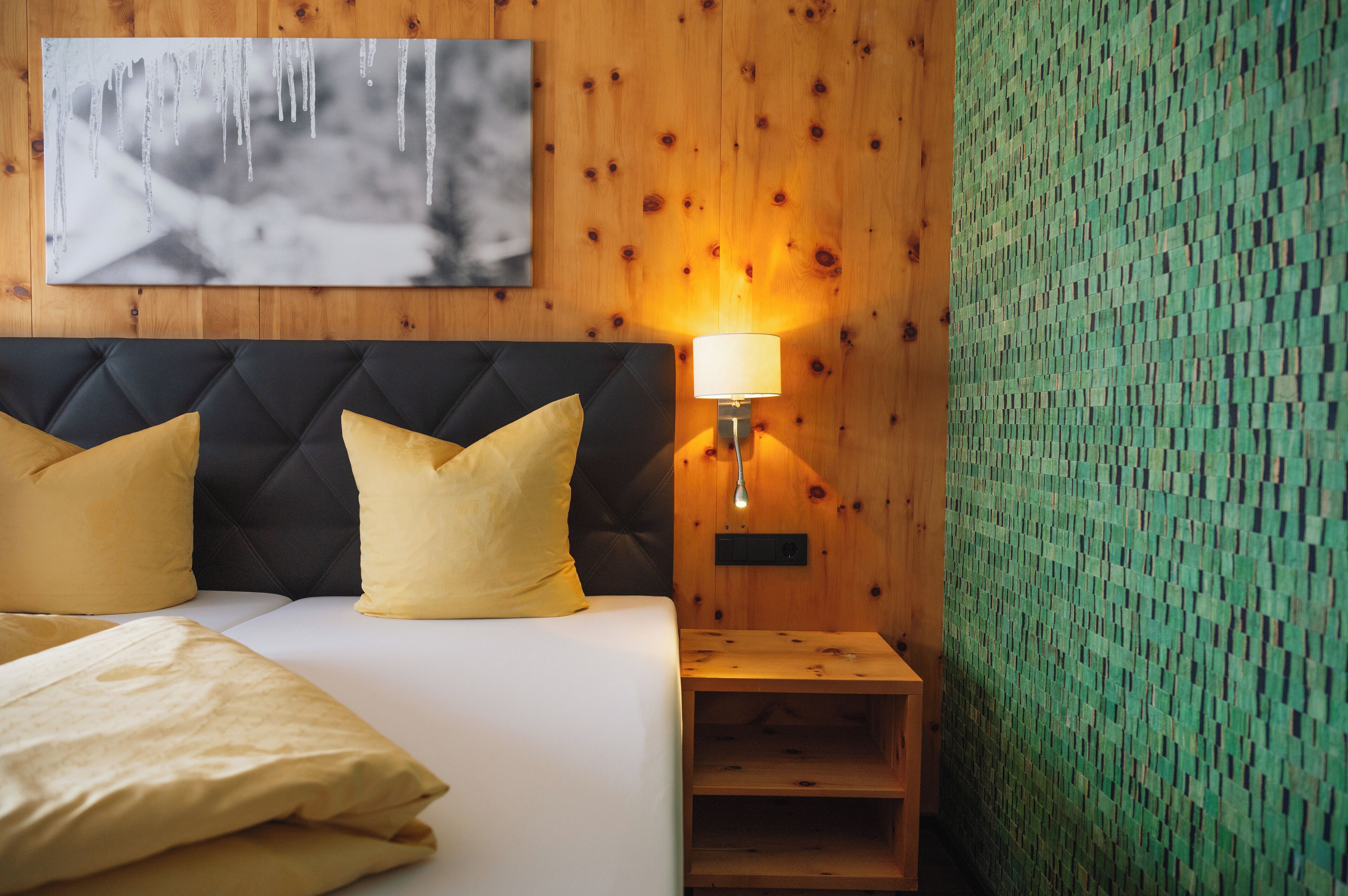 A bedroom with a tufted headboard, a bedside table with a lamp, and a wall-mounted artwork.