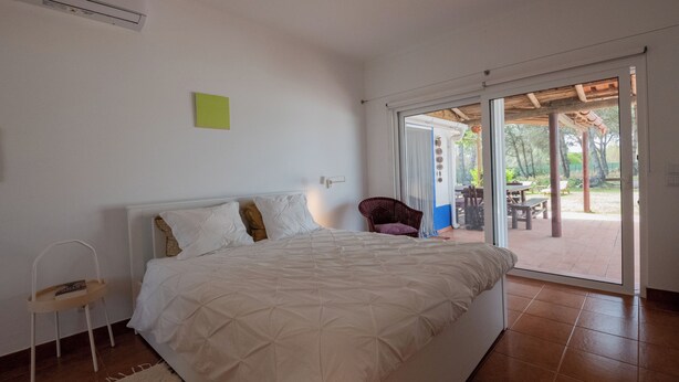 Une chambre avec un lit, une chaise et une porte-fenêtre coulissante donnant sur une terrasse extérieure.