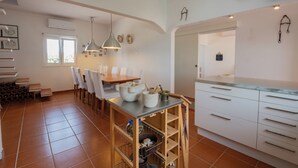 Une cuisine spacieuse avec un coin repas, des meubles blancs et un sol carrelé.
