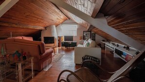 Un espace de vie chaleureux aménagé dans les combles, avec des poutres apparentes, un canapé, une table basse et une bibliothèque.