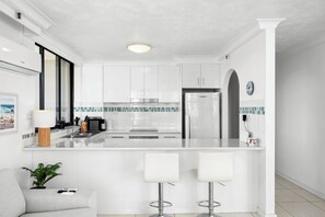A modern kitchen with white cabinets, a central island with bar stools, and a tiled backsplash. - Cosy Ocean Views Apartment w/cinema at night. Pet-Friendly! (Surfers Paradise)