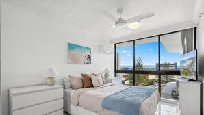 Ein modernes Schlafzimmer mit Bett, Nachttischen, Deckenventilator und einem großen Fenster mit Blick auf die Stadt.