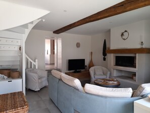 Ein modernes Wohnzimmer mit einer Couch, Sesseln, einem Fernseher und einem Kamin.